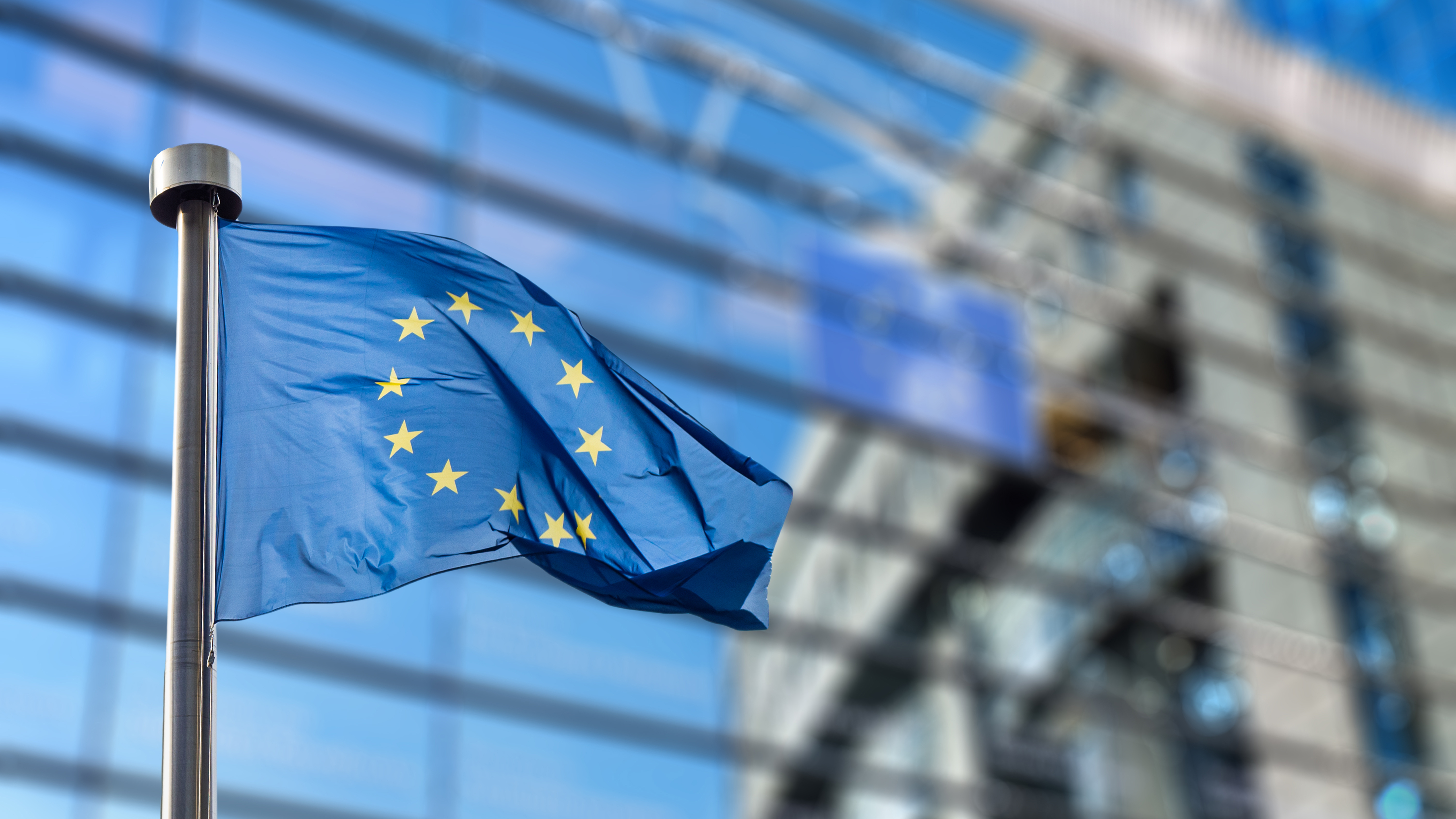 European Union flag waving in front of a modern glass building