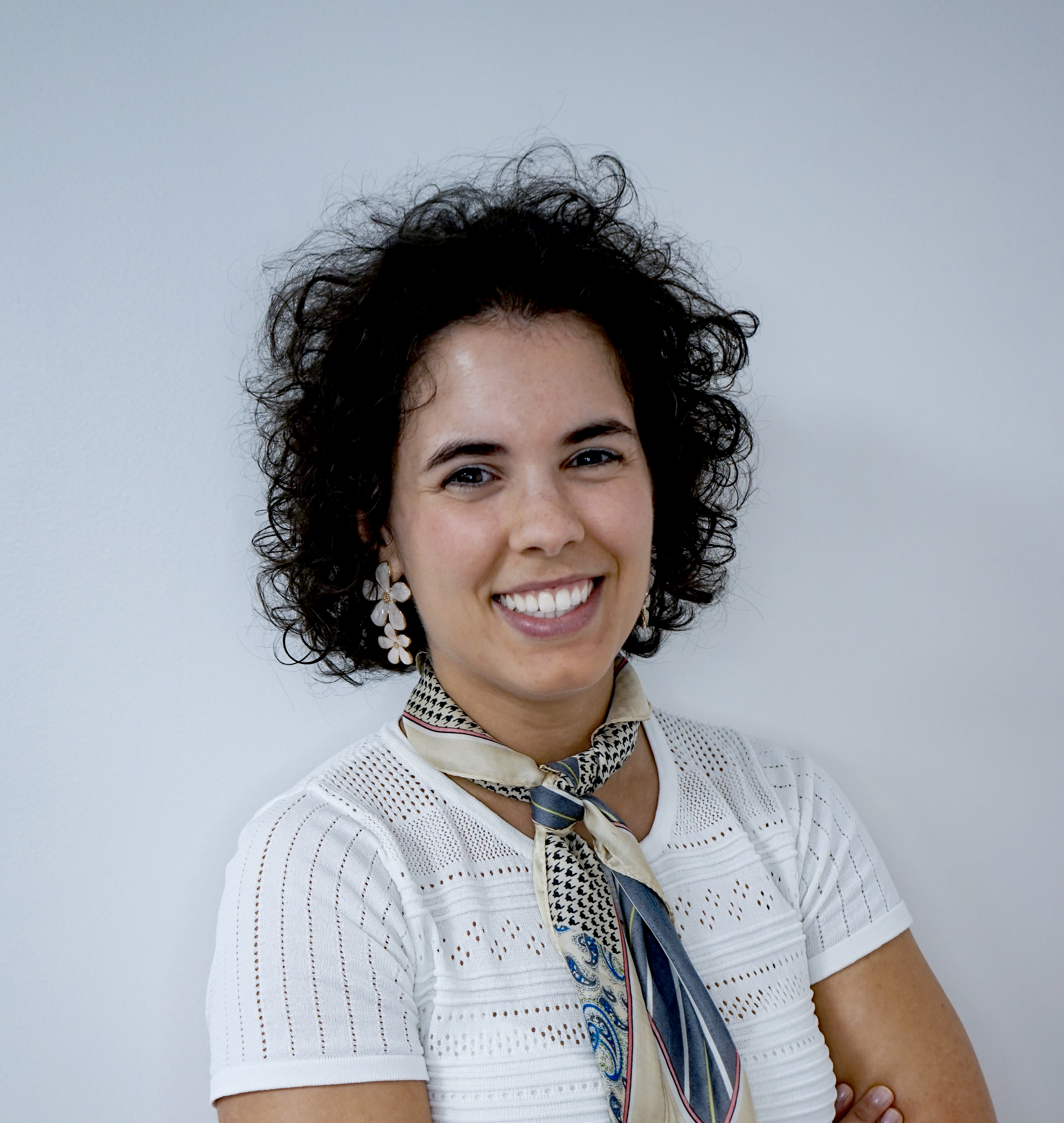 Smiling Kiwa employee from Kiwa Portugal wearing white top with a patterned scarf and earrings against a light background