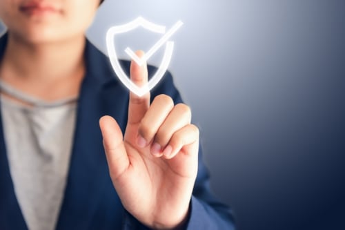 Person touching a digital shield icon with a checkmark, representing cybersecurity or data protection