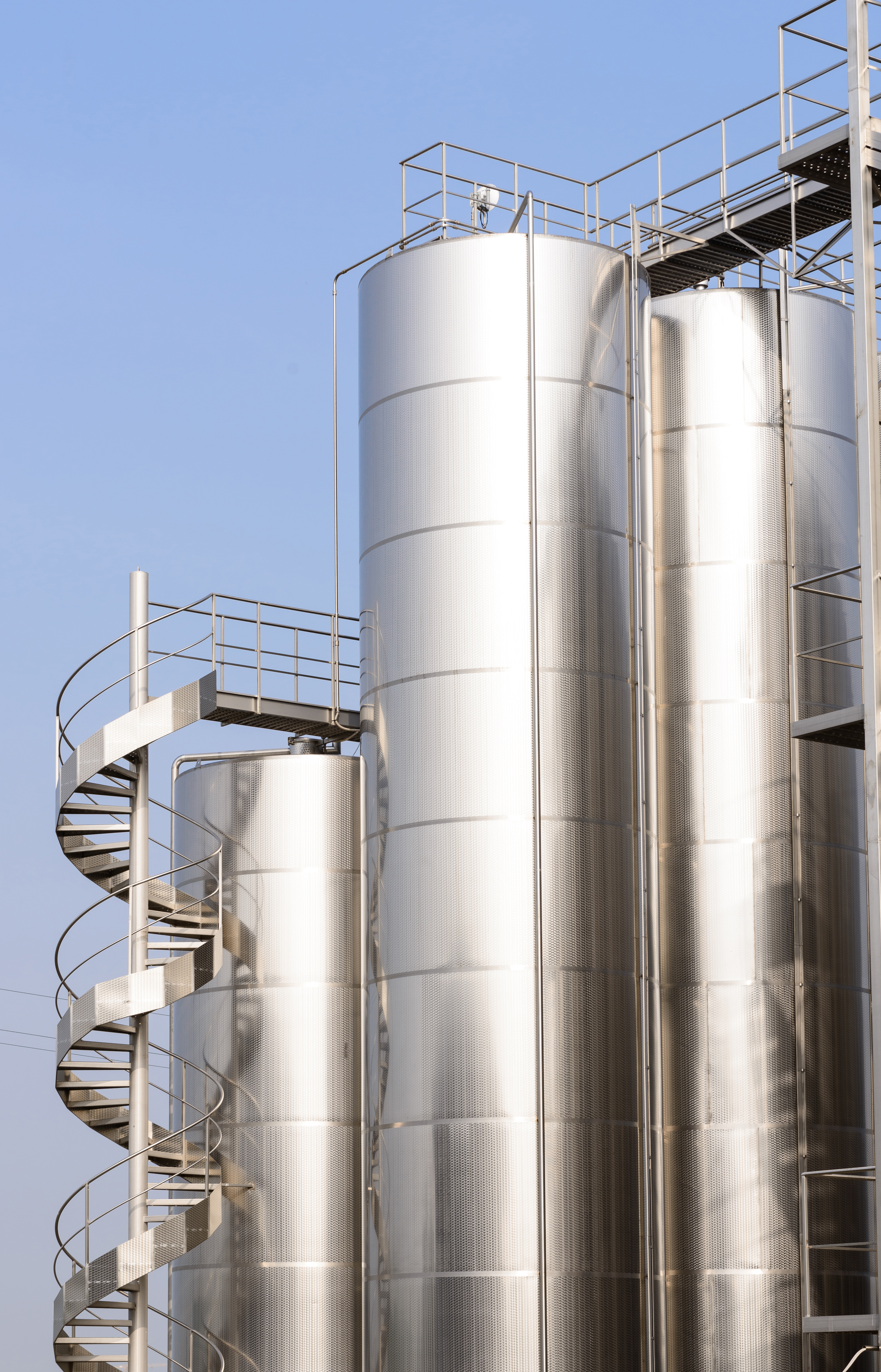 Kiwa inspected stainless steel industrial silos with a spiral staircase, against a clear blue sky, showcasing modern architectural design in industrial storage