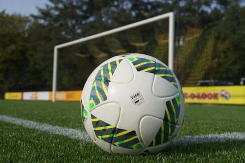 Close-up of a FIFA-approved soccer ball on a green field with a goalpost in the background