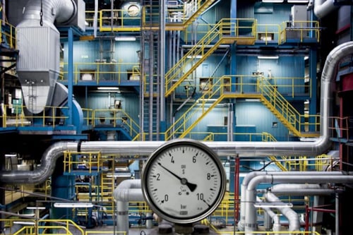 Industrial facility with pipes and a pressure gauge in the foreground.