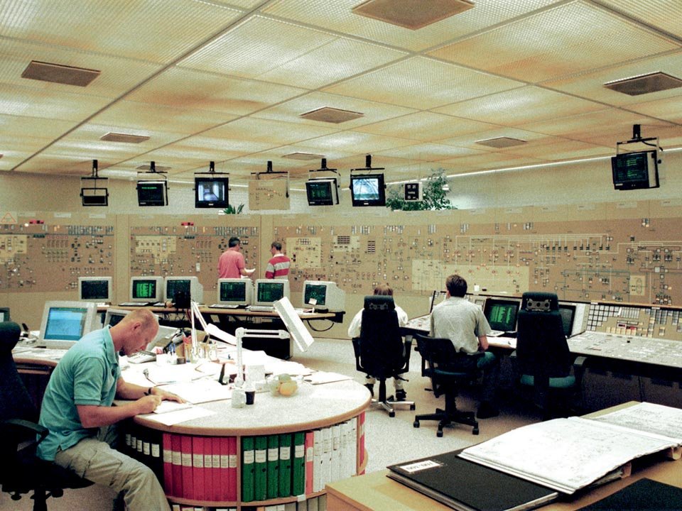 Control room with multiple operators working at desks, surrounded by computer monitors and control panels, in a high-tech facility