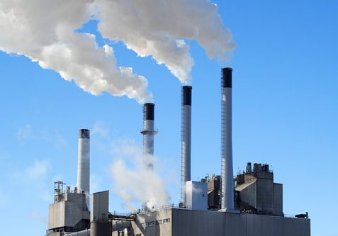 Industrial power plant with four smokestacks emitting white smoke against a clear blue sky