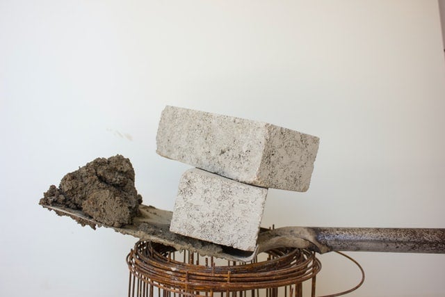 two grey CE-marked cement blocks on top of a shovel, which is on top of rolled-up wires