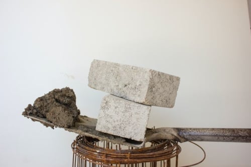 two grey CE-marked cement blocks on top of a shovel, which is on top of rolled-up wires