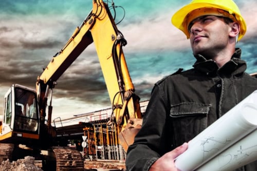 Construction site with excavator and confident worker in hard hat and holding blueprints, cloudy sky background