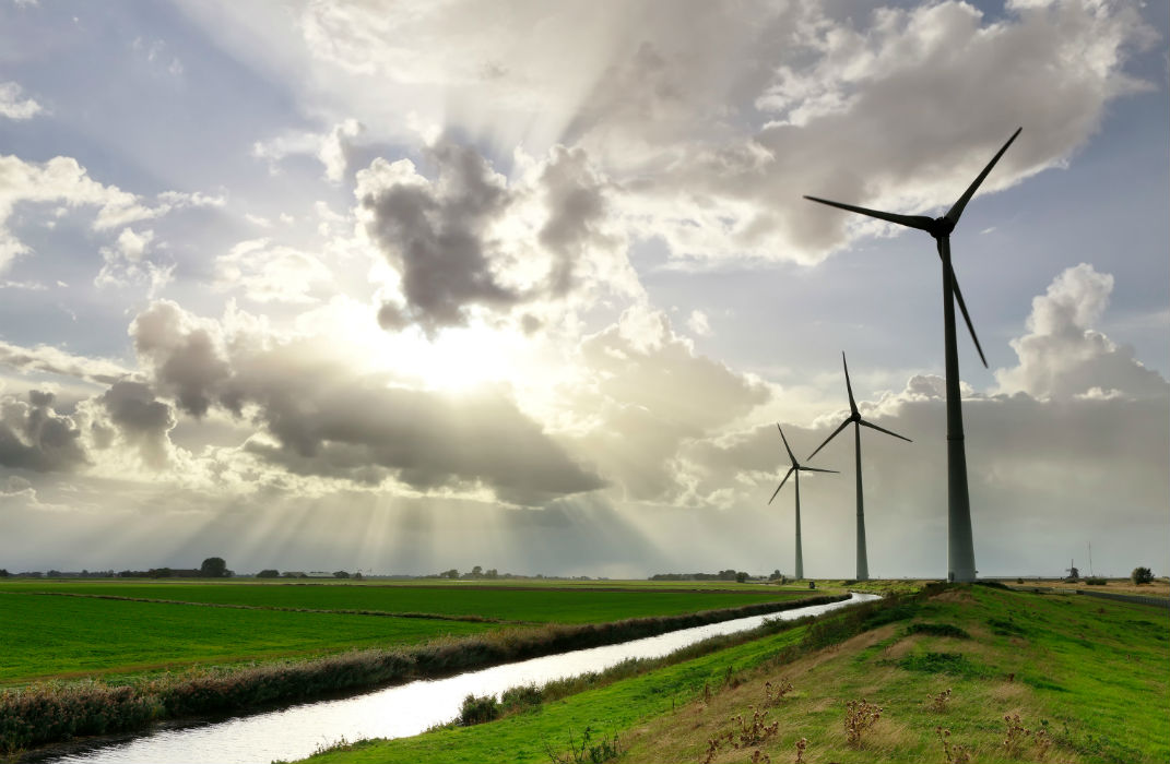 open sunny field with three wind turbines next to a canal