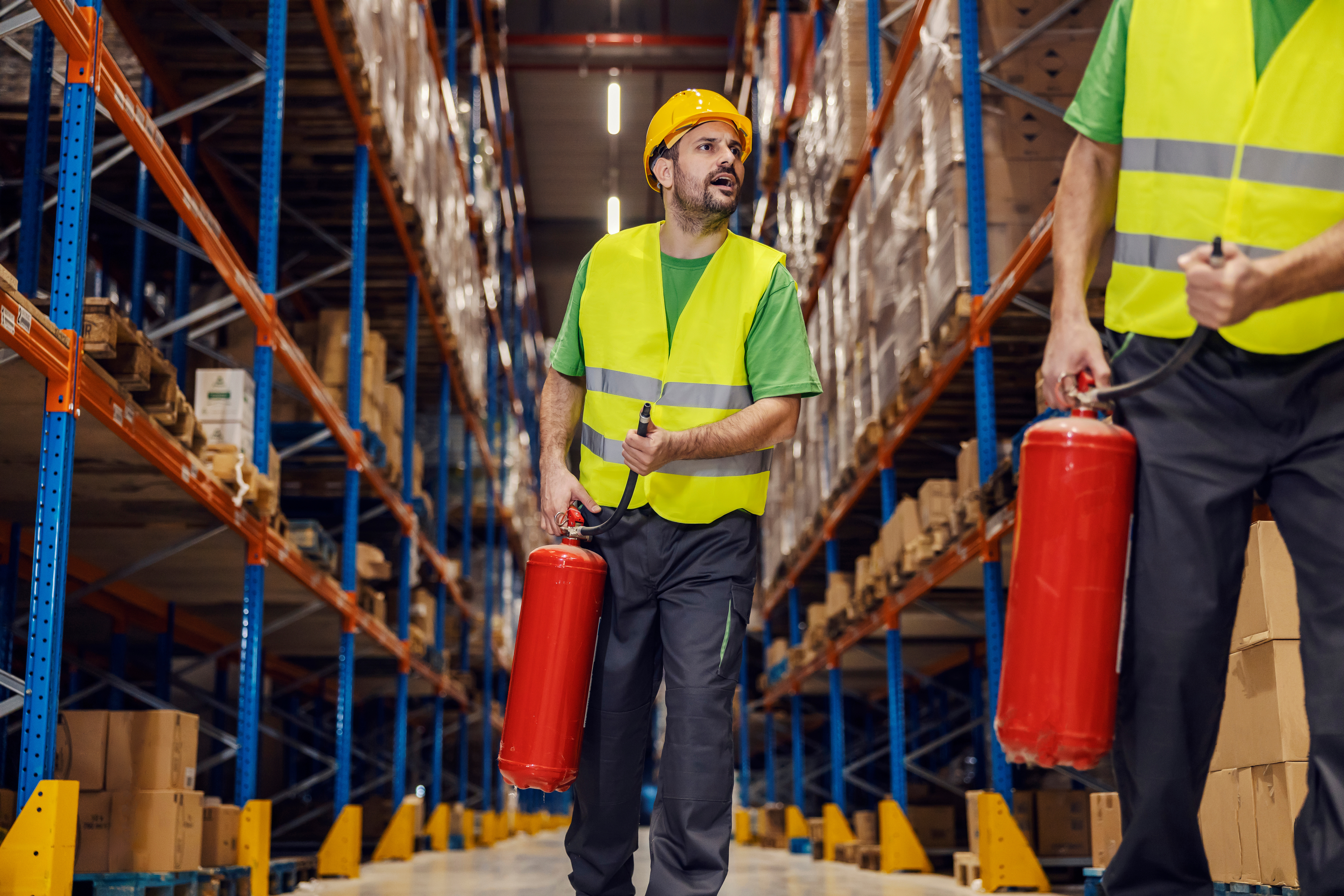 Workers in safety gear holding  fire extinguishers in a warehouse aisle, emphasizing safety protocols and emergency preparedness