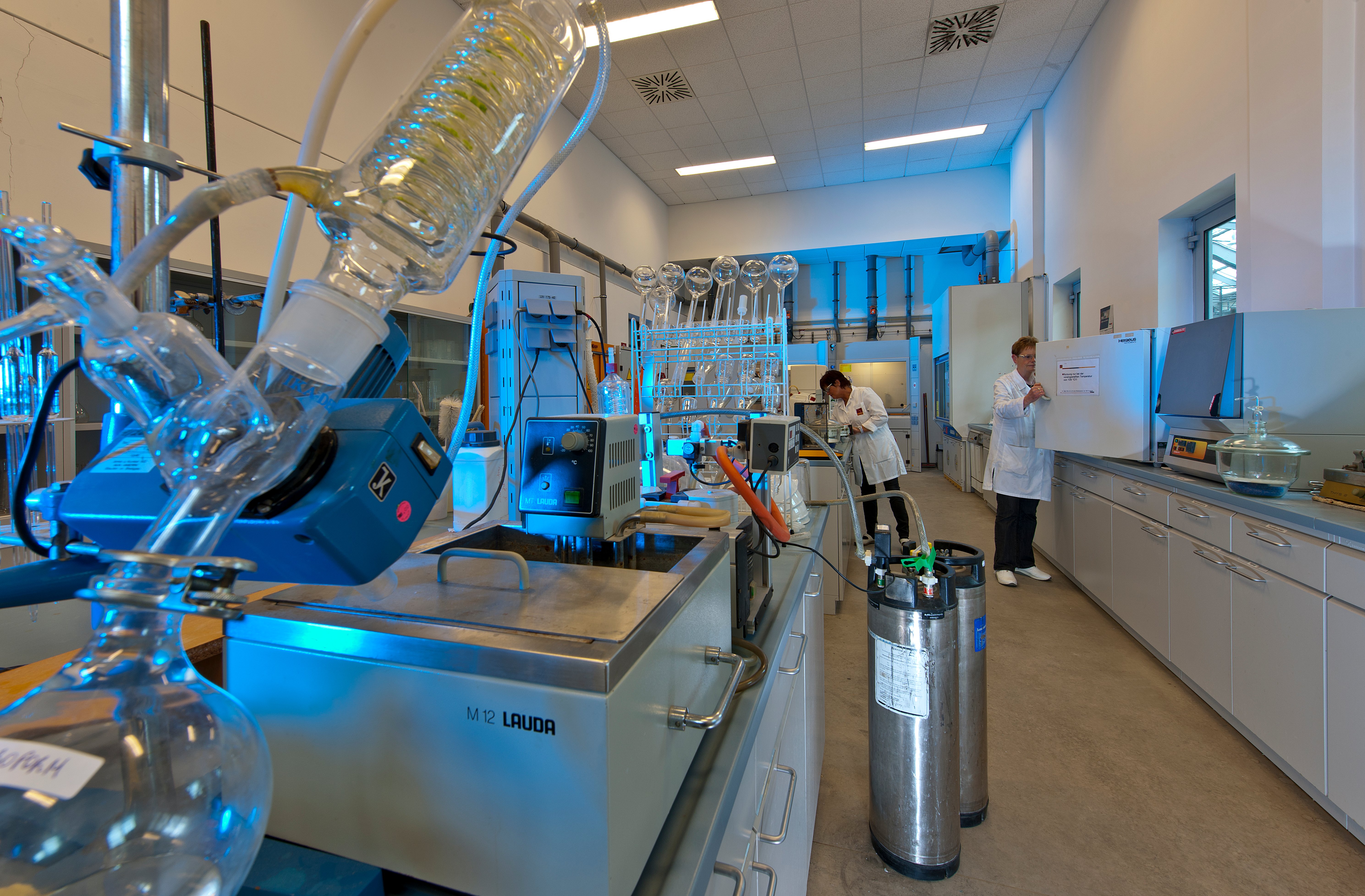 Modern chemistry laboratory with advanced equipment and Kiwa laboratory employees conducting experiments. The lab features distillation apparatus and storage tanks, showcasing a professional research environment