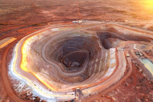 Aerial view of a large open-pit mine at sunset, showing terraced earth layers and surrounding barren landscape in a remote area