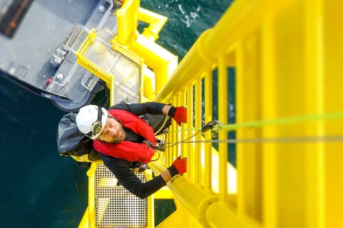 man climbing the stairs to the top of a floating windmill in the sea