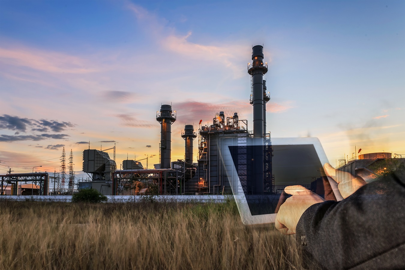 Person using a tablet in front of a power plant during sunset, showcasing technology and industrial infrastructure