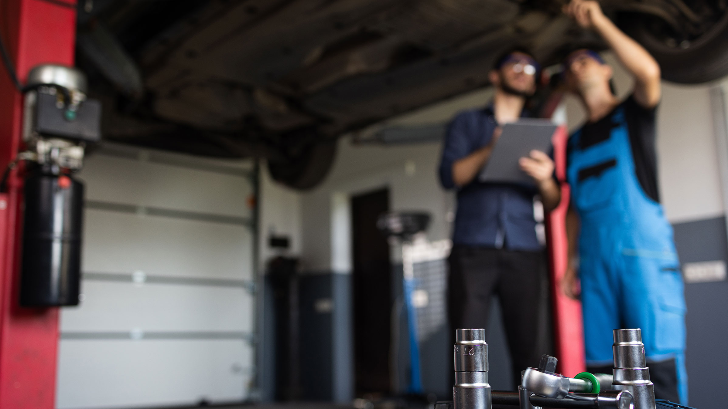 Bilmekaniker arbetar med en personbil, motorhuven är öppen. 