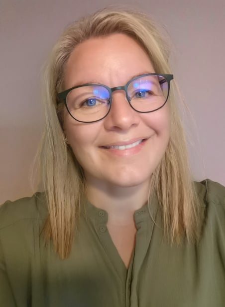 Torill Strand, Kiwa employee, with blonde hair and glasses wearing a green blouse against a neutral background