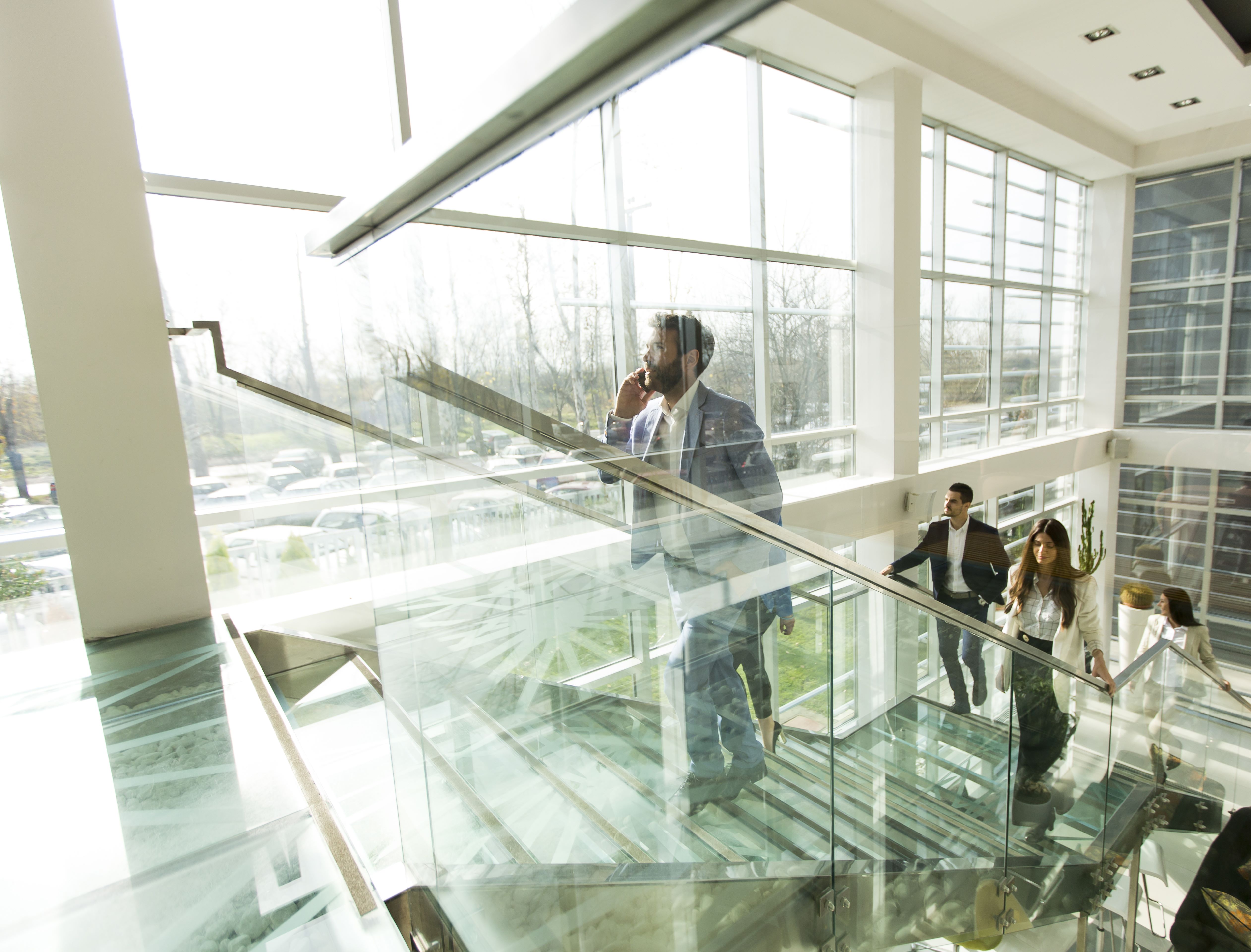 Business professionals walking up a glass staircase in a modern office building with large windows and natural lighting