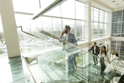 Business professionals walking up a glass staircase in a modern office building with large windows and natural lighting