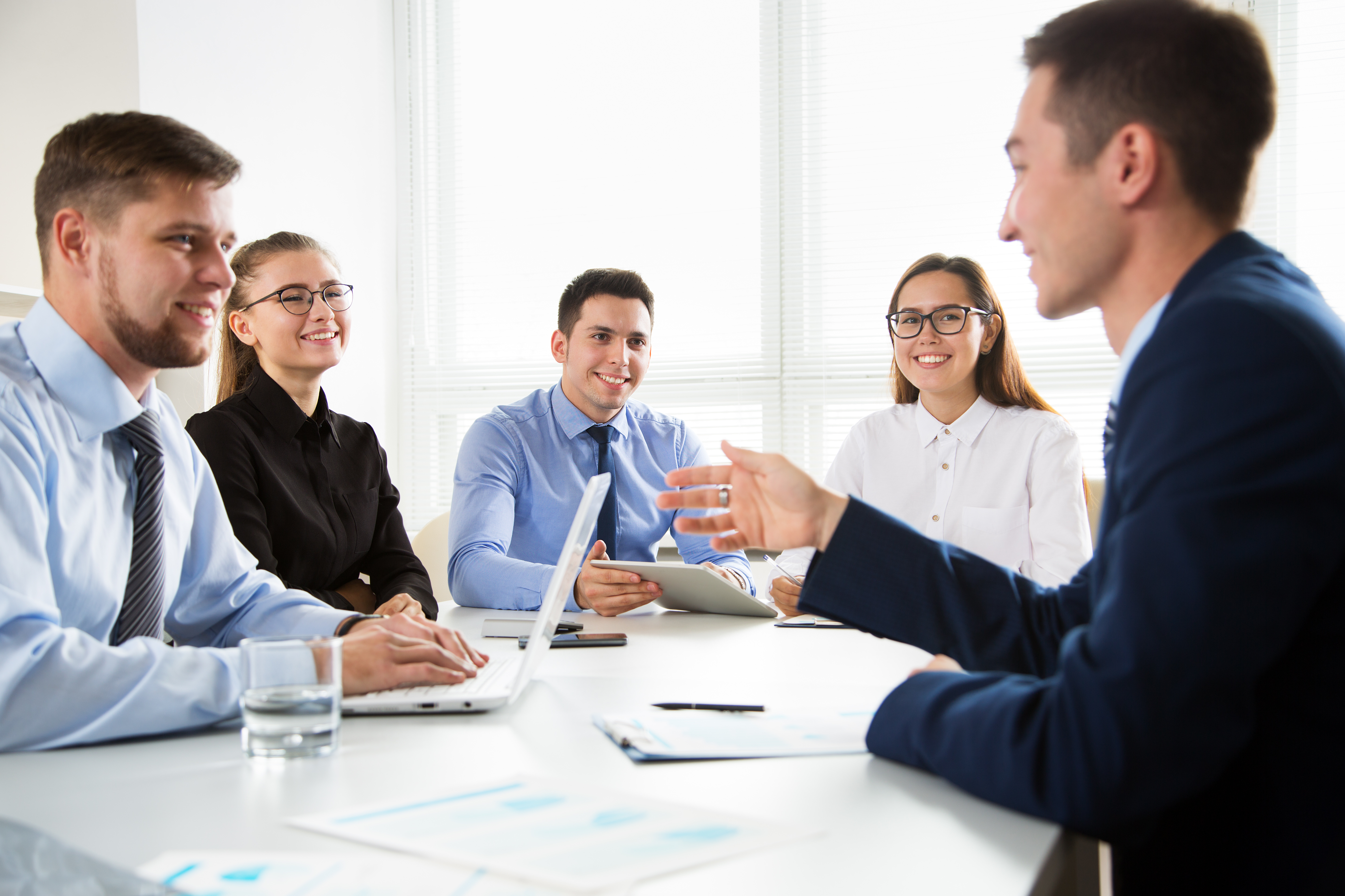 A diverse group of business professionals engaged in a meeting around a conference table, with laptops and documents